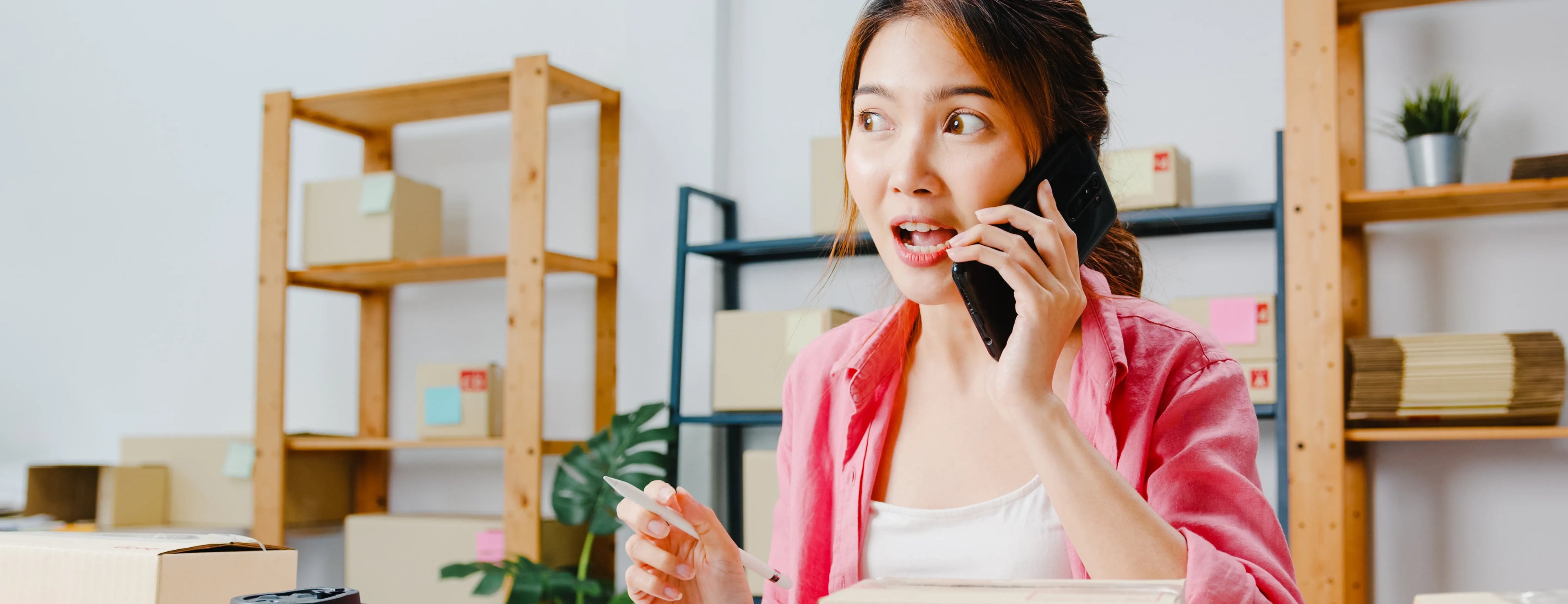 Woman talking on a phone in an office setting with shelves and plants in the background