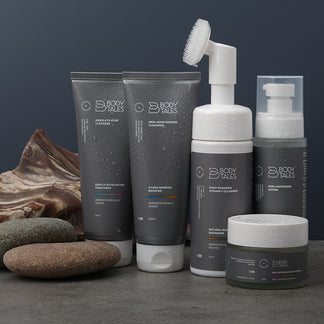 Set of skincare products including bottles, jars, and a brush on a dark surface with a stone background.